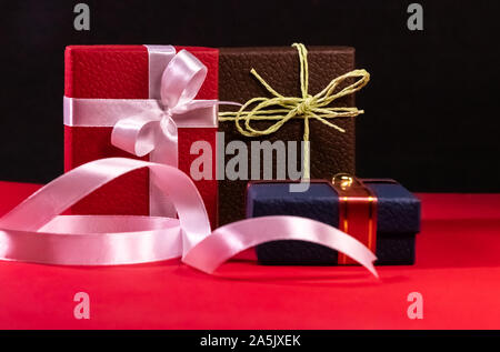 Drei dekorierten Braun, Rot und Blau Geschenkboxen mit schönen Bänder und Bögen auf rote Fläche und schwarzen Hintergrund Stockfoto