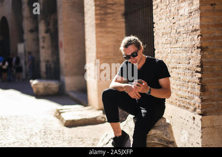 Junge männliche Tourist können Sie über Smartphone im Kolosseum in Rom, Italien. Stockfoto