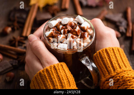 Tasse heiße Schokolade mit Marshmallows, Zimt und Schokolade Soße in weibliche Hände. Detailansicht. Komfort Essen für Herbst und Winter Stockfoto