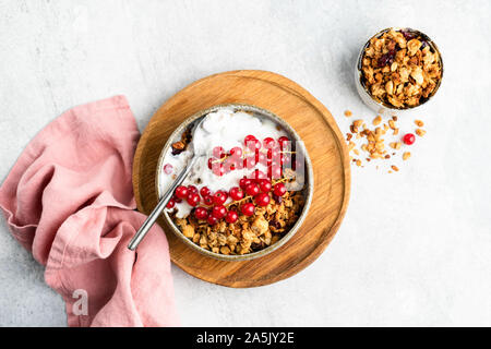 Frühstück Cerealien Hafer Müsli mit Joghurt und Rote Johannisbeere Beeren auf grauem Beton Hintergrund. Tabelle Ansicht von oben. Gesundes Frühstück essen, saubere Essen con Stockfoto
