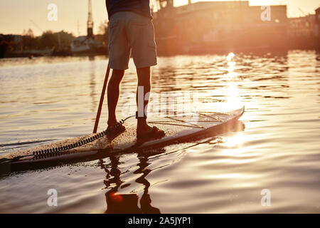 Mann stand auf paddleboard am Fluss in der Dämmerung, Schuß von hinten Stockfoto