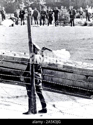 Oktober 1961-kommunistischen "Polizisten" (volkspolizist), stehen zwischen den Grenzzaun und Wand, bereitet eine Tear-Gas Granate bei einer Gruppe von West-berliner, die auf Ihrer Seite der Grenze versammelt die Roten Garden zu Jeer zu werfen Stockfoto