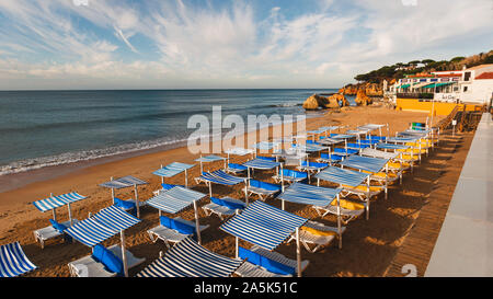 Sonnenliegen und bereit für Touristen auf der Praia Dos Olhos D'Agua in der Algarve an der Südküste von Portugal an einem warmen Sommermorgen Stockfoto