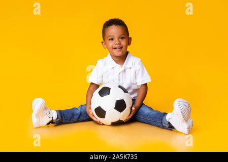 Portrait von niedlichen kleinen Jungen mit Fußball-Sitzung über Gelb studio Hintergrund Stockfoto