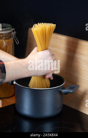 Spaghetti in den Topf mit kochendem Wasser, männliche Hände Haufen Nudeln kochen Pan in der modernen Küche Stockfoto