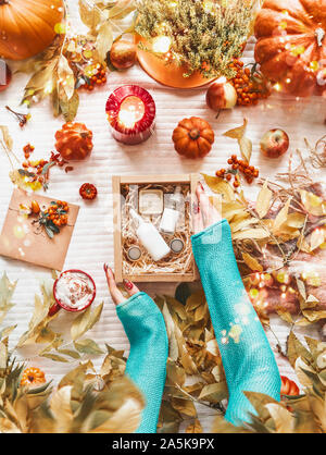 Weibliche Hände box Holding mit kosmetischen Mitteln auf dem Desktop mit Herbstlaub, Kürbisse, brennende Kerzen und Tasse heiße Schokolade oder Kaffee. Hautpflege r Stockfoto