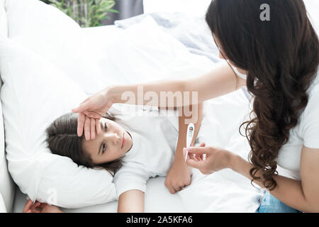 Sick cute Teen Girl im Bett zu liegen, während ihre Mutter sitzt in der Nähe und prüft die Temperatur mit dem termometer am Morgen Stockfoto