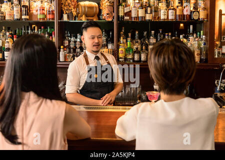 Zwei junge Frauen und Barkeeper an Theke Stockfoto