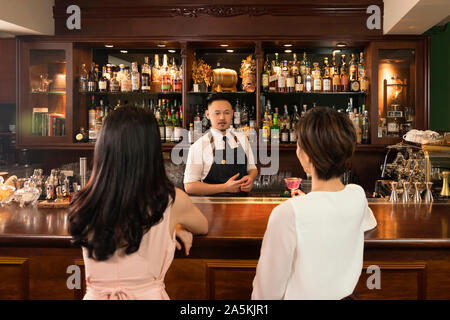 Zwei junge Frauen und Barkeeper an Theke Stockfoto