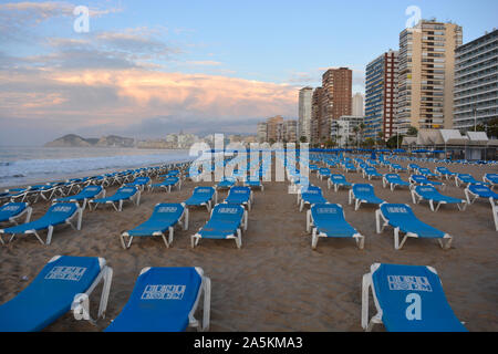 Reihen von leeren blauen Liegestühle und Sonnenschirme am Strand Playa de Levante Strand, sehr früh am Sonntagmorgen im Oktober, Benidorm, Alicante, Spanien Stockfoto