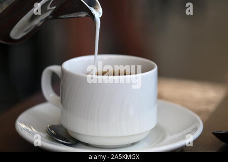 Gießen Milch/Sahne von einem silbernen Metall kann in eine frische Tasse Kaffee am Morgen. Wunderbare Art, einen Tag zu beginnen! Der Kaffee ist voller Energie! Stockfoto