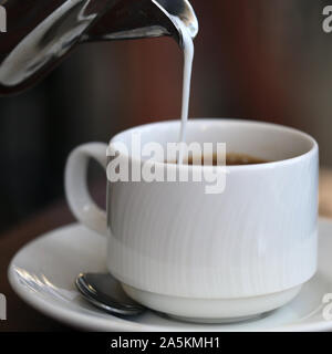 Gießen Milch/Sahne von einem silbernen Metall kann in eine frische Tasse Kaffee am Morgen. Wunderbare Art, einen Tag zu beginnen! Der Kaffee ist voller Energie! Stockfoto