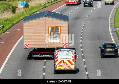 HANSON, Wide Load Escort Vehicle; Spedition Delivery Trucks, Spedition, LKW, Transport, LKW, Fracht, MAN Vehicle, statische Caravans Lieferung, Transport, Industrie, Supply Chain Fracht, Lasten überhängend am Heck des Fahrzeugs; Lasten überhängend Seite des Fahrzeugs, auf der M6 in Lancaster, Großbritannien Stockfoto