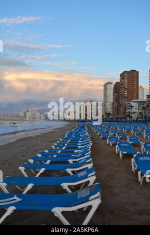 Reihen von leeren blauen Liegestühle und Sonnenschirme am Strand Playa de Levante Strand, sehr früh am Sonntagmorgen im Oktober, Benidorm, Alicante, Spanien Stockfoto