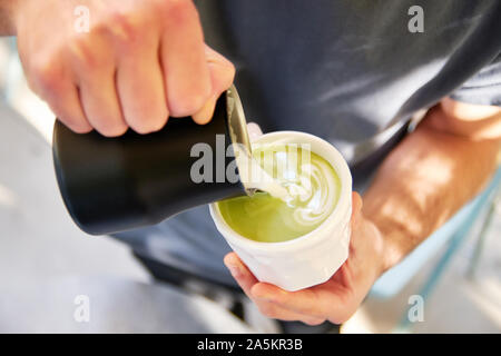 Männliche Barista, vegan Matcha Cappuccino mit hafermilch mit latte Kunst im Café im Freien. Stockfoto