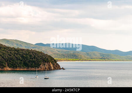 Zwei yahts Floating in der Nähe der malerischen Landschaft von Cala Violina Strand im Tyrrhenischen Meer Bucht, die von grünen Wald in der Provinz von Grosseto in der Toskana umgeben Stockfoto