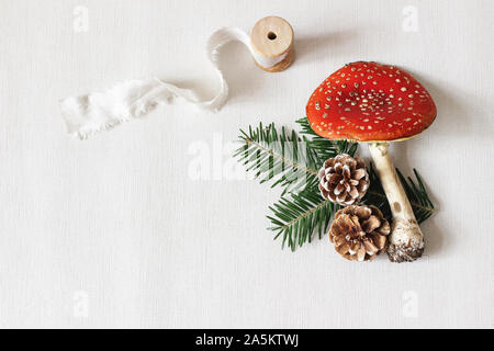 Weihnachten festlich gestalteten Stoffzusammensetzung. Red fly agaric Pilz, Seidenband, Tannenzapfen und Tannenbaum Äste auf weißen Hintergrund. Winter t Stockfoto