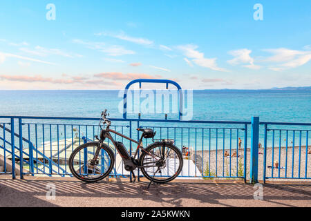 Ein Fahrrad steht an einer Geländer auf der Promenade des Anglais mit dem türkisfarbenen Wasser der Bucht der Engel hinter in Nizza, Frankreich. Stockfoto