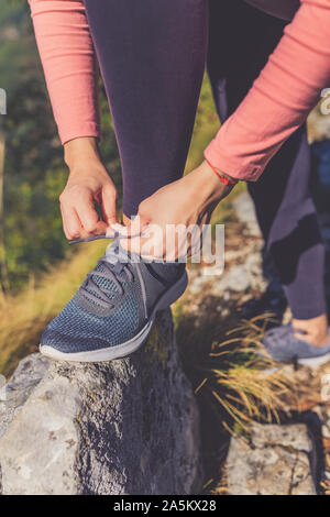 Sportlich aktive Frau in Sportkleidung kniend auf Rock und binden Schnürsenkel. Morgen Training in der Natur. Stockfoto