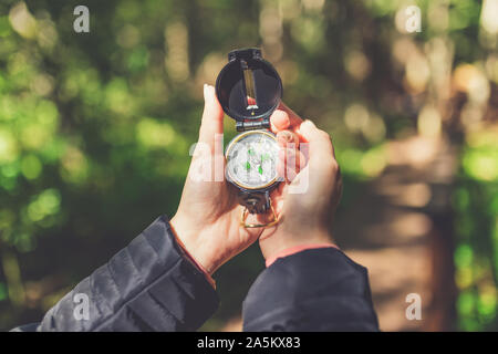 In der Nähe der weiblichen Händen hält Kompass gegen Wald Fußweg. Natur Orientierung Konzept. Stockfoto