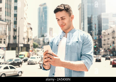 Freizeitaktivitäten im Freien. Stilvolle Kerl stehen auf der Straße grasen Smartphone lächelt glücklich Stockfoto