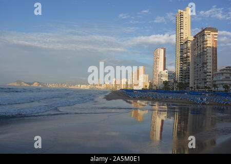 Reihen von leeren blauen Liegestühle und Sonnenschirme am Strand Playa de Levante Strand, sehr früh am Sonntagmorgen im Oktober, Benidorm, Alicante, Spanien Stockfoto