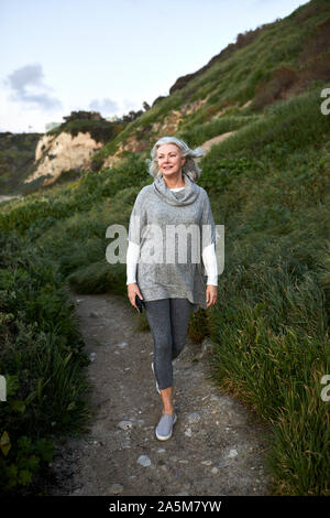 Die volle Länge der älteren Frau zu Fuß auf Fußweg am Manhattan Beach bei Sonnenuntergang Stockfoto