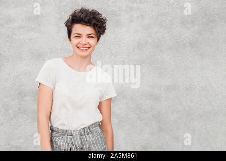 Charmante junge Frau mit kreativen Frisur ist lächelnd und mit freudiger Happy Face posieren. Emotionen und Gefühle. Stockfoto