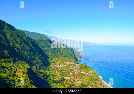 Schönen Nordküste der Insel Madeira, Portugal. Sao Jorge Village inmitten grüner Hügel und tropischer Wald umgeben, Felsen durch den Atlantischen Ozean. Blick von der Spitze des Hügels. Touristische Ort. Stockfoto