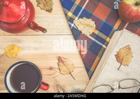 Heißen Tee, warme Decke, Apple, Blätter im Herbst und Buch auf alten hölzernen Hintergrund, Vintage Farben Foto. Ansicht von oben, flach. Stockfoto