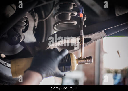 Auto master Mechaniker Werkstatt Heizung die Schrauben mit Butangas Schlag mini Schweißbrenner Flammenwerfer Brenner im Fahrzeug Reparatur Service Stockfoto