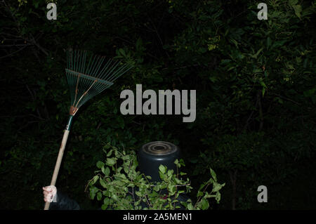 Eine geheimnisvolle Gestalt mit einem Topf auf dem Kopf und lässt über seinen Körper hält eine alte Blätter Rechen. Stockfoto