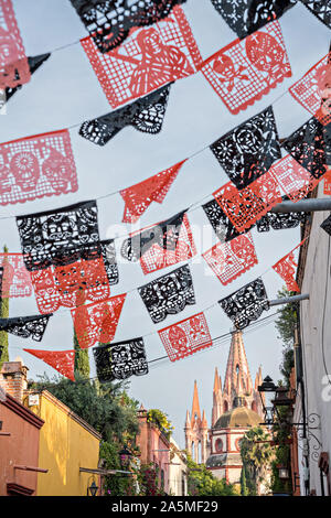 Kuppeln und Turmspitzen der Parroquia San Miguel Arcangel Kirche durch Papier Banner genannt Papel picado aufgereiht, der Tag der Toten Festival auf Aldama Straße im historischen Bezirk von San Miguel de Allende, Mexiko zu feiern gesehen. Stockfoto