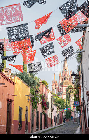 Kuppeln und Turmspitzen der Parroquia San Miguel Arcangel Kirche durch Papier Banner genannt Papel picado aufgereiht, der Tag der Toten Festival auf Aldama Straße im historischen Bezirk von San Miguel de Allende, Mexiko zu feiern gesehen. Stockfoto