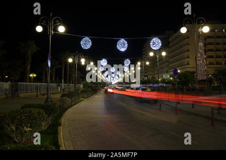 Nacht Stadtbild von Larnaca, Zypern, Straße mit Weihnachten beleuchtete Dekorationen wie hängenden Kugeln, rotes Licht Wanderwege durch das Fahrzeug verlassen. Stockfoto