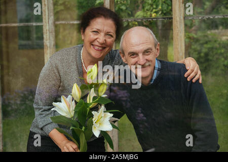 Alte glückliches Paar mit Blumen in einem gläsernen Gewächshaus in der Nähe von Summer House Stockfoto