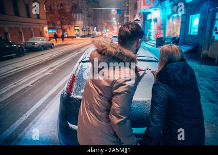 Junge erwachsene Paare zieht ein Herz auf schneebedeckten Auto Stockfoto