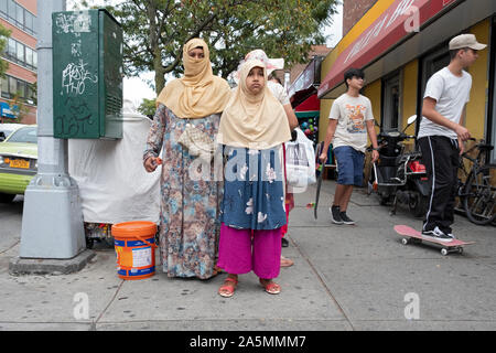 Eine Straßenszene in Jackson Heights mit 2 Frauen in traditionellen muslimischen Kleid und ein junger Mann auf einem Skateboard. In Queens, New York City. Stockfoto