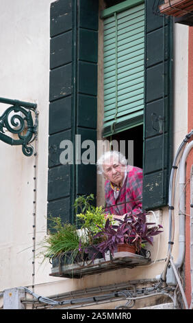 Eine ältere Venezianische Frauen tief in Gedanken wie schaut sie aus ihrem Fenster im Campo Marina in Venedig, Italien. Stockfoto