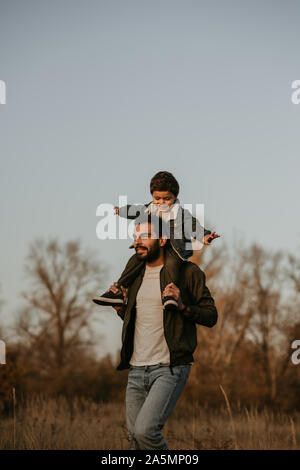 Gerne Vater Sohn Fahrt auf seinen Schultern, während auf dem Land gehen. Stockfoto