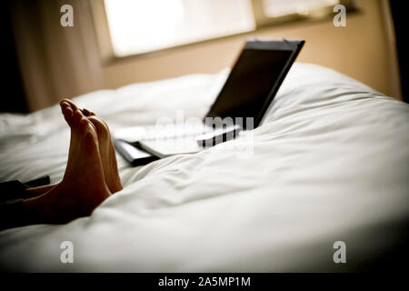 Füße auf ein Bett mit einem Laptop. Stockfoto