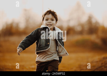 Glückliche junge in Jean jacket lächelnd und laufen auf Gras auf Herbst Feld. Stockfoto