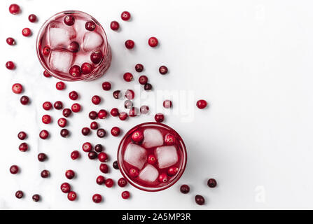 Cranberry Cocktail in Kristall Gläser mit Eis mit Beeren auf weißem Hintergrund hellem Marmor dekoriert. Kopieren Sie Platz. Flach Stil. Stockfoto