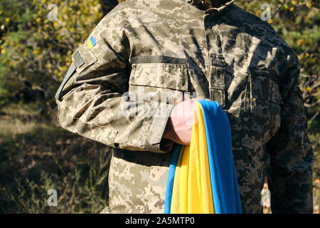 Ukrainische Soldaten hält in seiner Hand das gelb-blaue Flagge des Staates, er presste seine Hand an seine Brust, Konzept der Erinnerung an die toten Soldaten Stockfoto