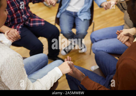 Hohen winkel Nahaufnahme des unkenntlich Leute sitzen ion Kreis und halten sich an den Händen während der Sitzung der Gruppe, cpy Raum Stockfoto