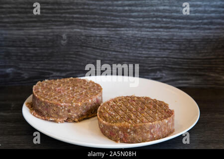 Einzelne weiße Platte mit frisch gepressten hausgemachten Burger Pastetchen. Das Sitzen auf dunklen Holzbank. Pattys sind gefüllt mit Speck und Käse Stockfoto