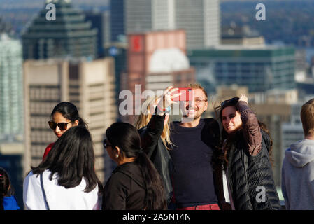 Drei Freunde unter selfies auf der Kondiaronk Belvedere auf Montreals Mont Royal, mit den Wolkenkratzern der Innenstadt über Stockfoto