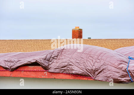 Wasserdichte tarp Abdeckung am Dach auf einem flachen, undicht, beschädigte Dach als Notfall, temporäre Haus Schutz ein Gebäude von der weiteren Regen Schäden zu speichern. Stockfoto