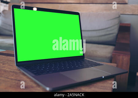 Mockup Bild der Laptop mit leeren grünen desktop Bildschirm auf hölzernen Tisch in modernen Loft Cafe Stockfoto