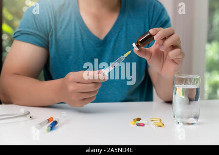 Junger Mann mit Injektionsnadel und Impfstoff in Hand mit sortierten pharmazeutische Medizin Pillen auf Tisch Stockfoto
